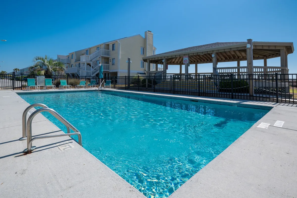 A relaxed outdoor recreation area with a sparkling swimming pool, sun loungers, and a gazebo set amidst greenery. The setting invites guests to sunbathe, swim, or gather for social time in a resort-like environment.