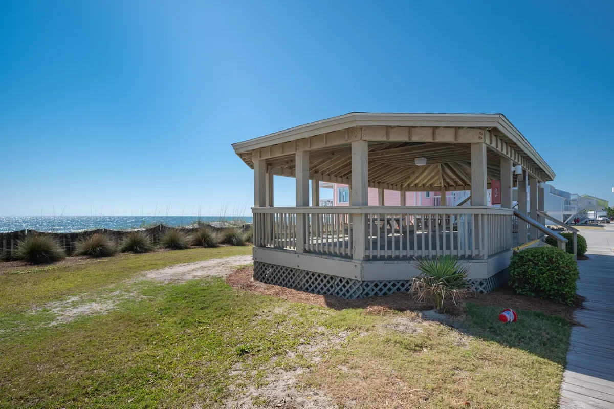 An exterior scene showcasing an open pavilion structure with panoramic ocean views and surrounding greenery, ideal for gatherings, yoga, or simply enjoying the coastal breeze. The cheerful mood and natural setting invite guests to explore the outdoors.