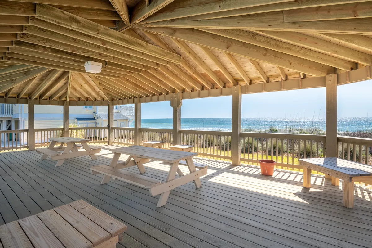 This image shows an exterior gathering area with wooden picnic tables and open space overlooking the ocean. The group-friendly setup invites guests to enjoy picnics, casual meals, or sunset celebrations together. The open-air atmosphere ties in with the idea of shared experiences in a coastal setting.