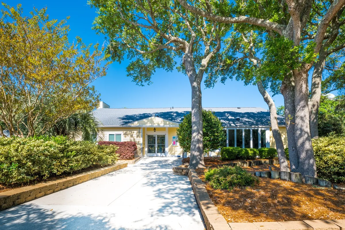 This image shows the property's front entrance framed by large trees and landscaped gardens. The clearly visible entry pathway leads to the building, suggesting a welcoming arrival experience.