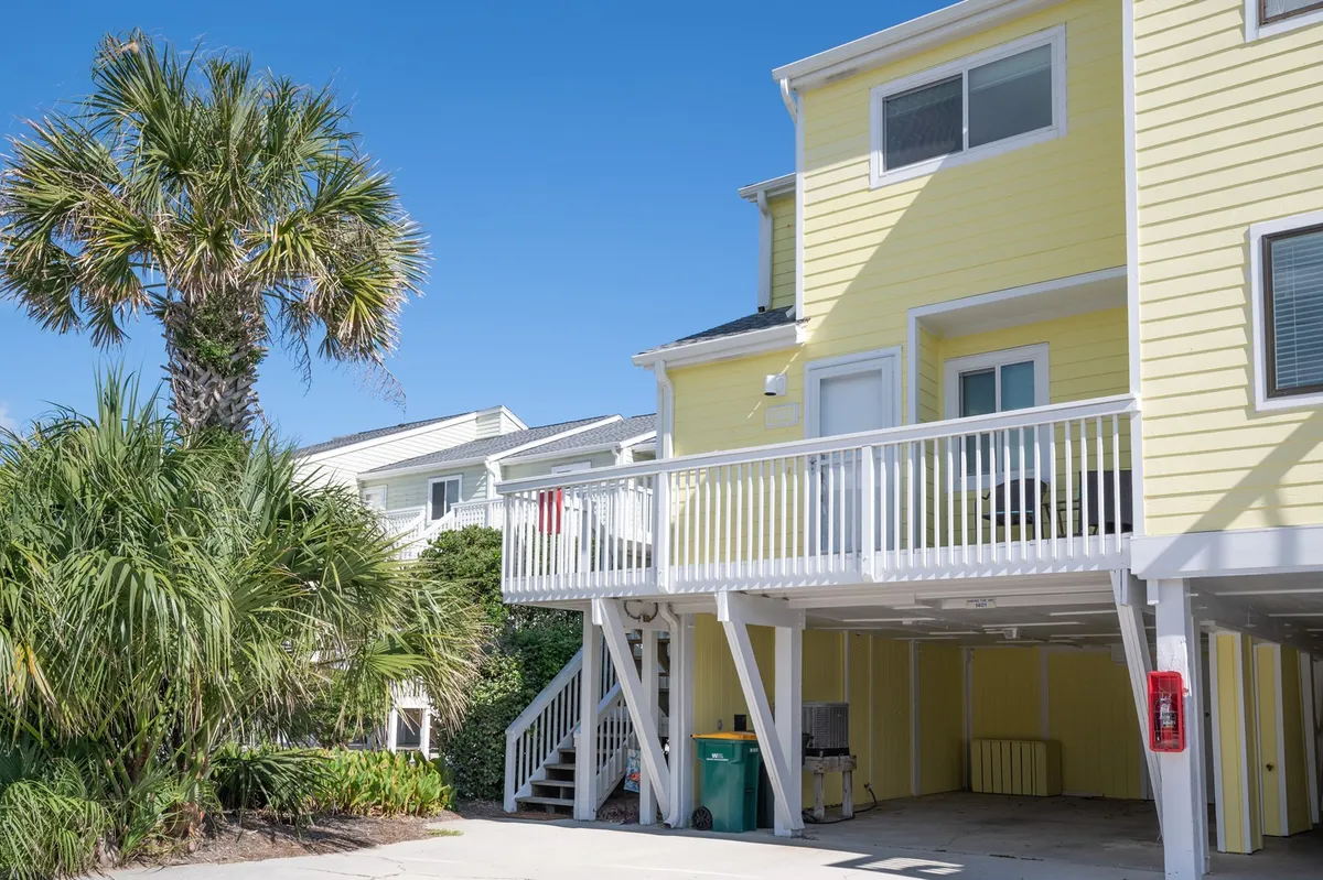 This image features the cheerful exterior of the yellow building, accented with palm trees and an inviting balcony. The scene hints at outdoor enjoyment and shared moments, with space for relaxing or socializing. The visible balcony embodies the idea of gathering together to enjoy the view and fresh air.