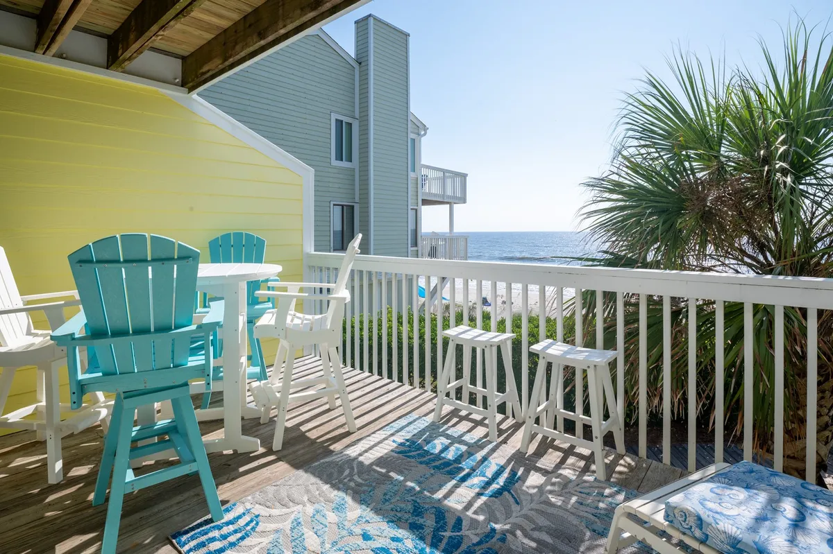 The image features a private oceanfront deck furnished with inviting deck chairs and a colorful rug, framed by a swaying palm tree, all overlooking the sparkling Atlantic. The setting exudes relaxation and is perfect for soaking in sunrise views, outdoor dining, or stargazing in the evening.