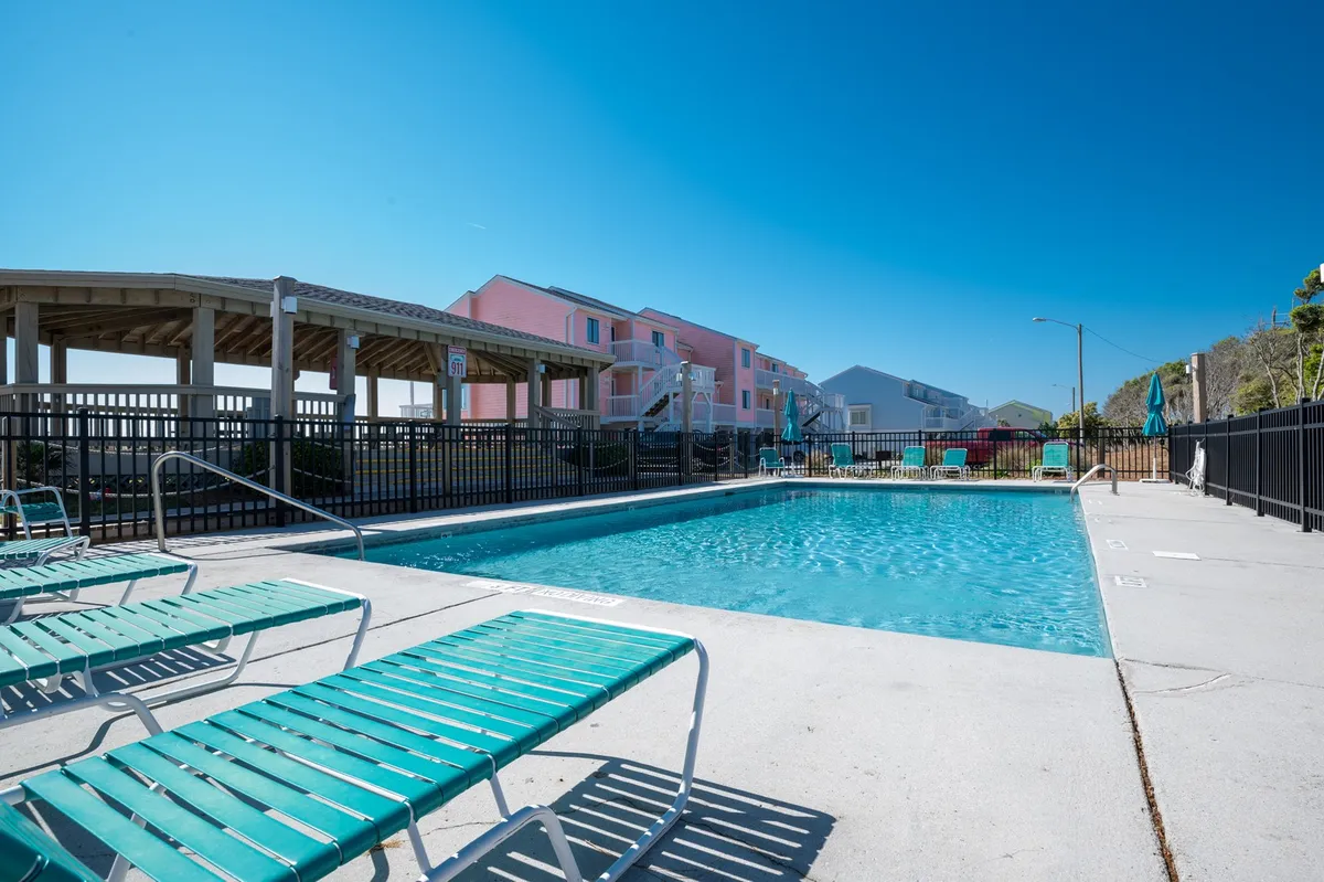 A sparkling outdoor swimming pool surrounded by sun loungers, nestled among the resort’s buildings. The scene is bright and inviting, with space for families to relax, swim, and enjoy sunny days together.