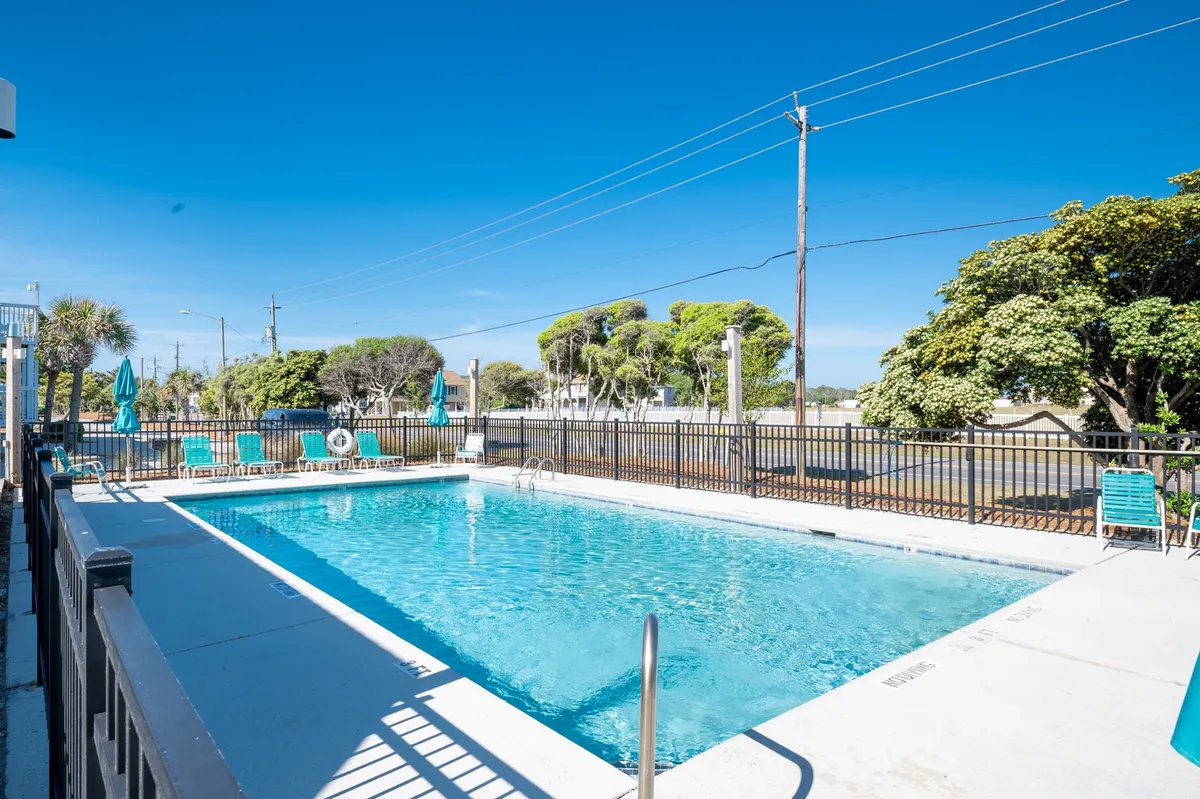 The image highlights a sparkling outdoor swimming pool flanked by lounge chairs and lush greenery, evoking relaxation and opportunities for fun under the sun. The setting suggests both activity and tranquility in a resort environment.