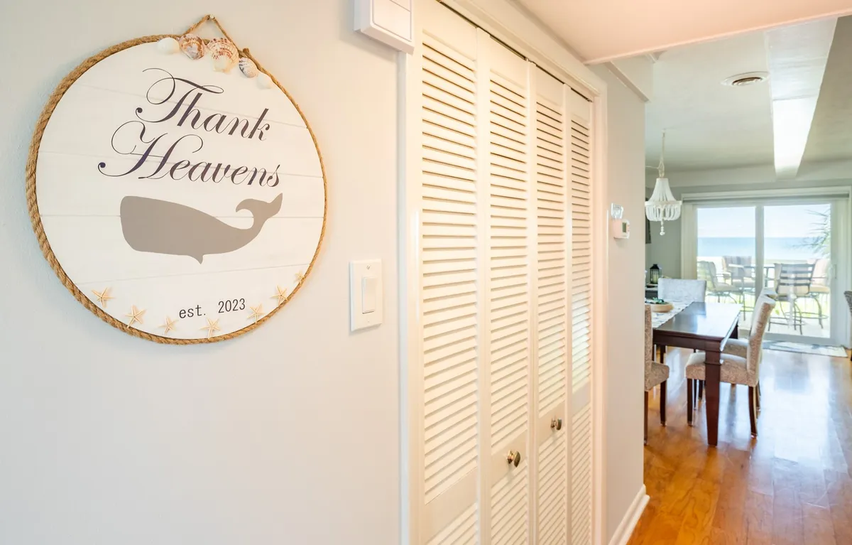 A naturally lit interior space featuring a decorative whale motif sign, folding doors that likely lead to storage (potentially the laundry closet or an entry closet), and a window streaming in daylight. The setting is serene and hints at organized, functional spaces.