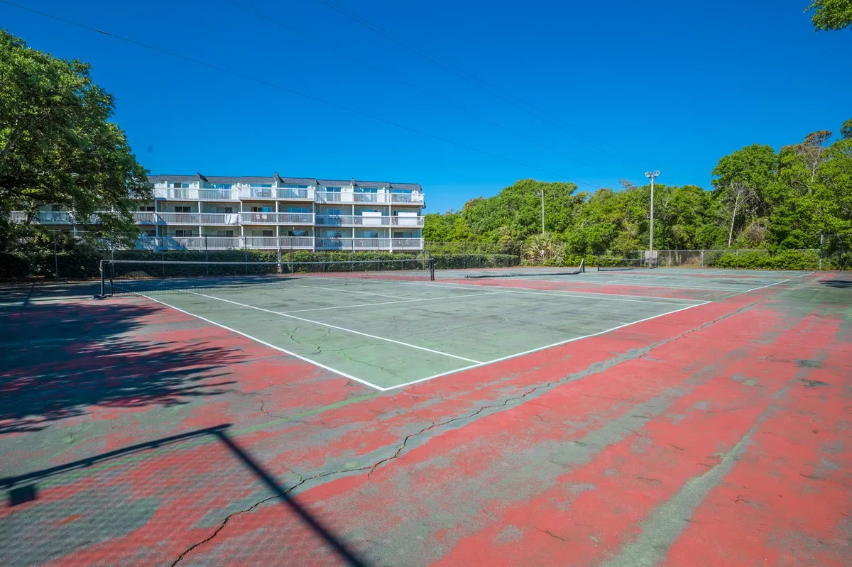 This exterior image features lively tennis courts surrounded by lush greenery, with players engaging in friendly matches and others relaxing by the court. In the background, an apartment building signals the resort setting and the sense of a vibrant community.