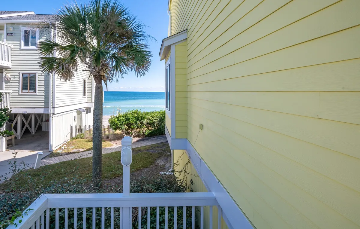 A tranquil view showcasing the yellow house exterior framed by a palm tree, with the ocean clearly visible in the background. The scene exudes peace and relaxation, hinting at direct access to the beach and the soothing sound of the waves.
