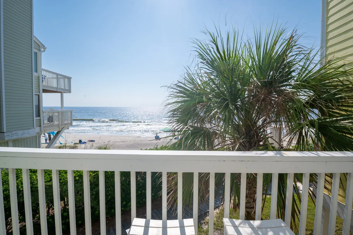 This image captures a stunning ocean view featuring a palm tree, sandy beach, and the boardwalk in the distance. The vantage point is from a balcony, reinforcing the connection between the home base and the attractions beyond. The tranquil setting suggests opportunities for both group outings and peaceful moments.